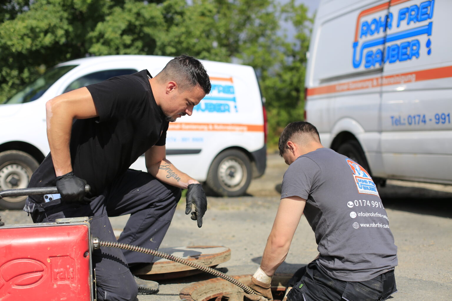 Zwei Mitarbeiter bei der Kanalreinigung, im Hintergrund zwei Firmenautos.